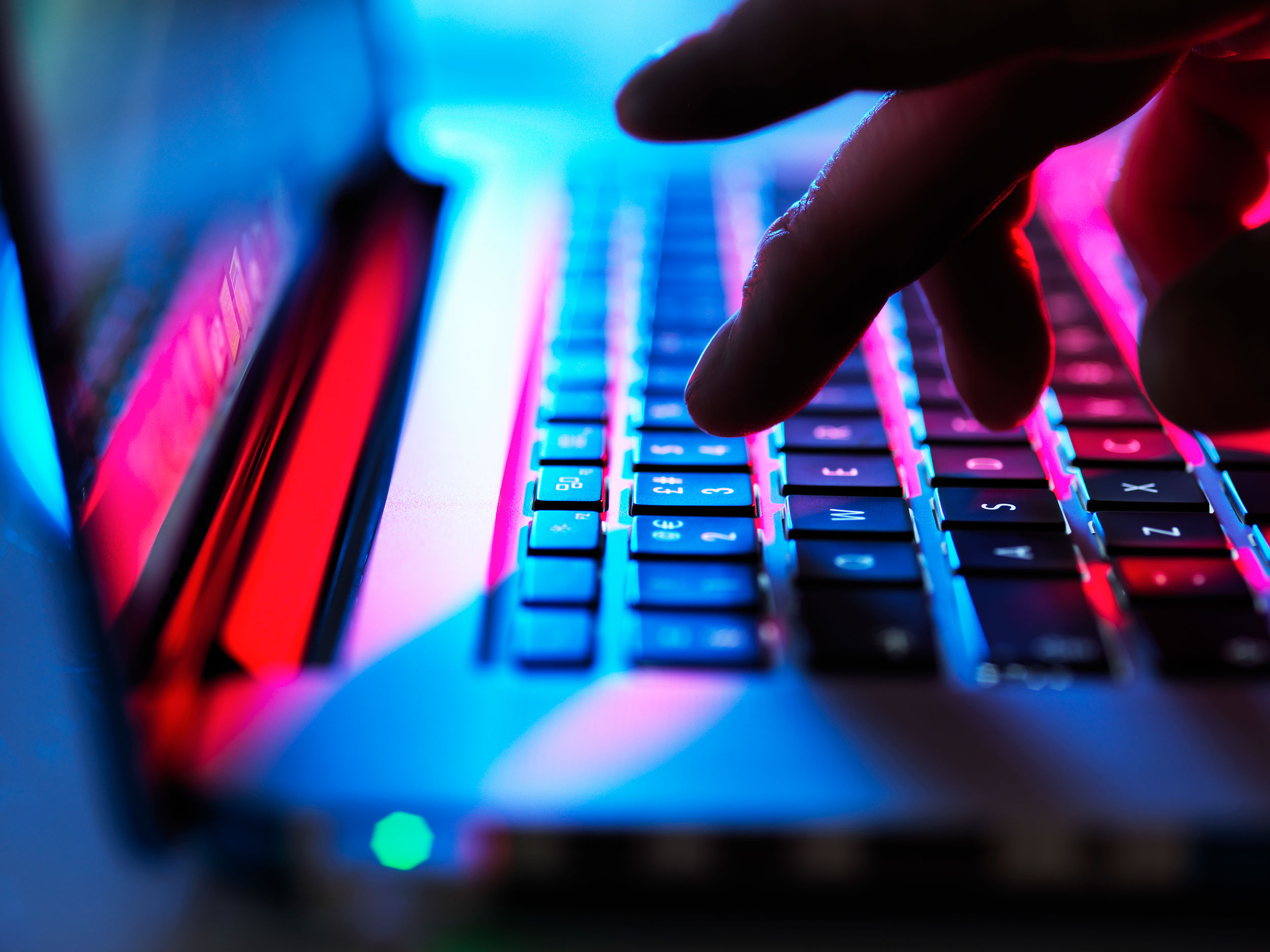 Fingers touch a laptop keyboard in eerie light
