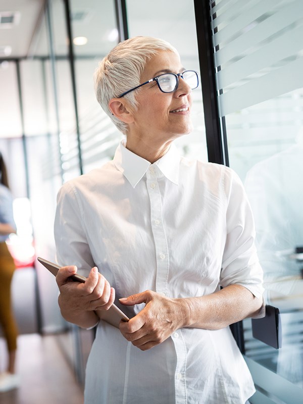 Older woman walking through office with her tablet.